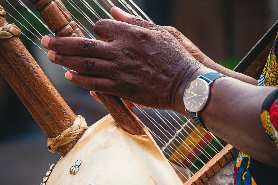 Mains d’un musicien jouant sur les cordes d’une kora, au-dessus de la calebasse