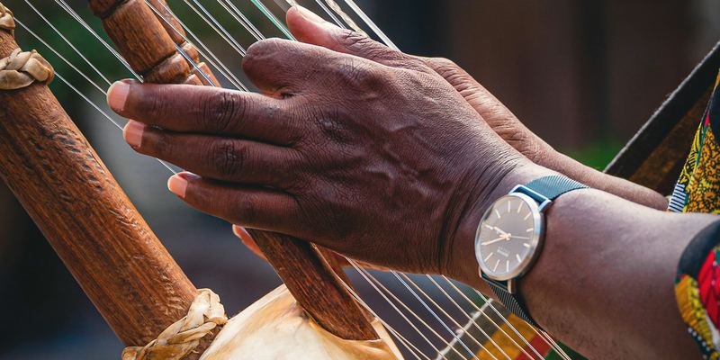 Mains d’un musicien jouant sur les cordes d’une kora, au-dessus de la calebasse
