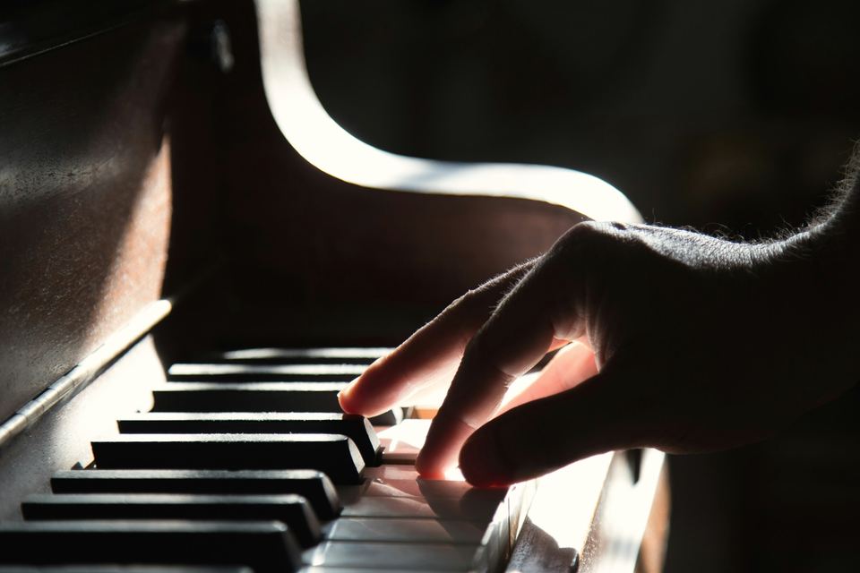 Main posée sur le clavier d’un piano, dans une lumière latérale chaude