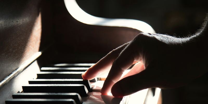 Main posée sur le clavier d’un piano, dans une lumière latérale chaude